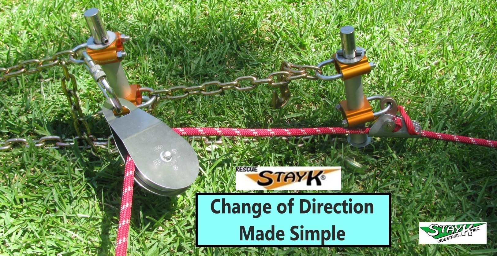 Pulley system for directing rope movements, featuring orange and silver components on grass. Highlights practical use in rescue operations.