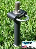 A durable, black steel stay kit anchor for sports equipment, featuring a top handle and a cylindrical base embedded in grass. Ideal for securing outdoor setups.