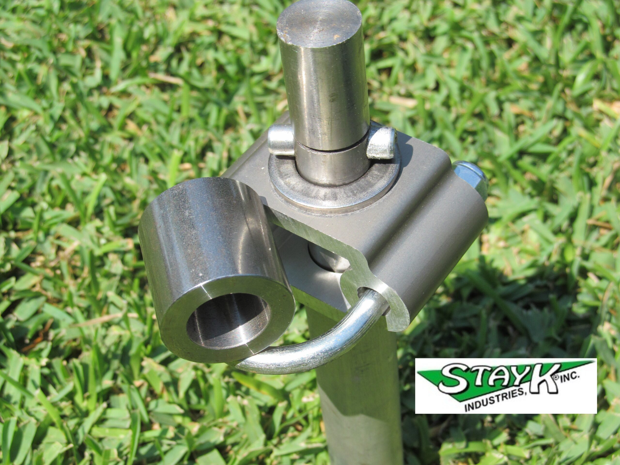 Metal bracket connector with a cylindrical attachment, set against green grass. Relevant for showcasing StayK Industries' innovative hardware solutions.