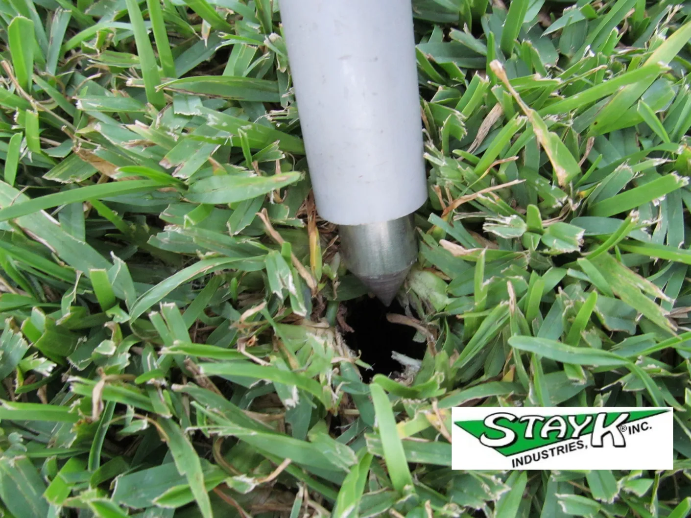 Soil aerator tool penetrating grass, creating a hole in the turf. Relevant for demonstrating lawn care techniques by Stay K Industries.