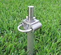 Stainless steel ground anchor with a loop and securing pin, embedded in green grass. Ideal for outdoor equipment and tent stabilization.
